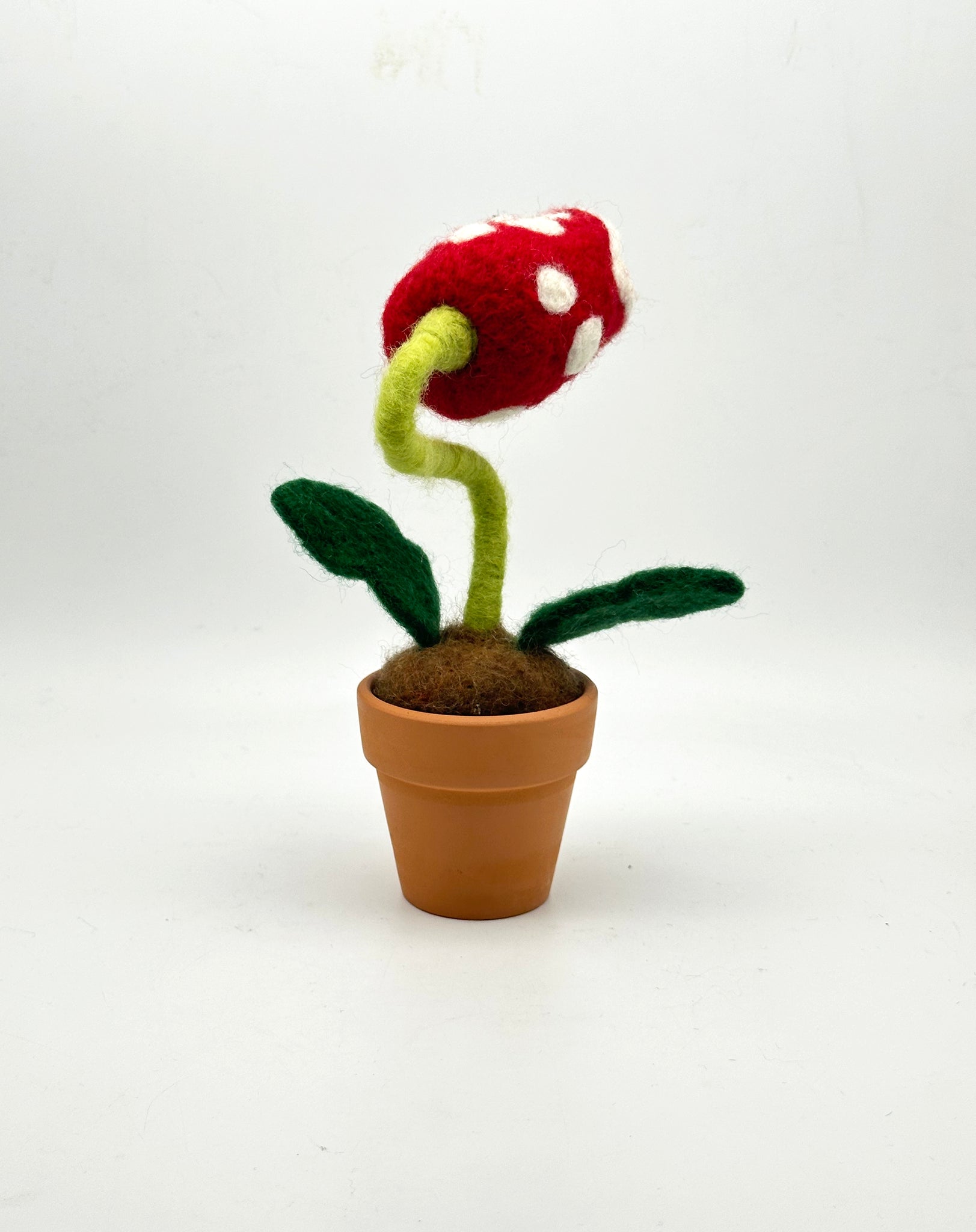 Needle felted plant in pot with red and white dotted head, white eyes and white teeth, from the back