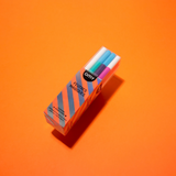 A boxed set of Omy Magic Fevers markers showing four colorful markers (blue, green, pink, and white) inside striped orange and gray packaging, set against a solid orange background.