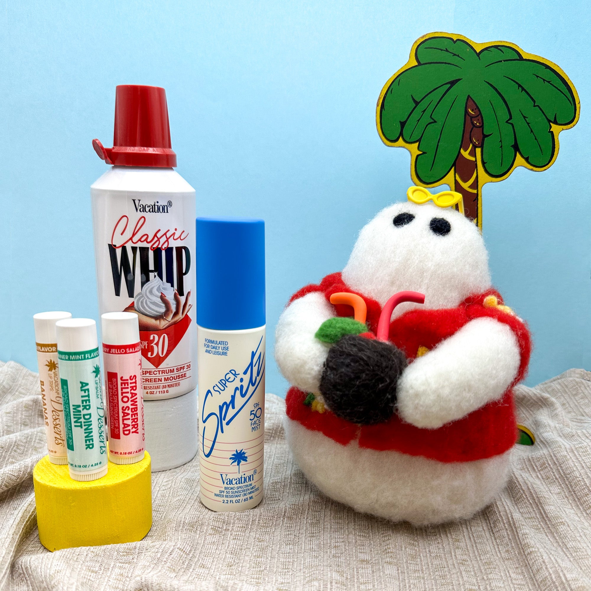 Hand felted small white ghost in a red Hawaiian style shirt holding a coconut cocktail, surrounded by beach props