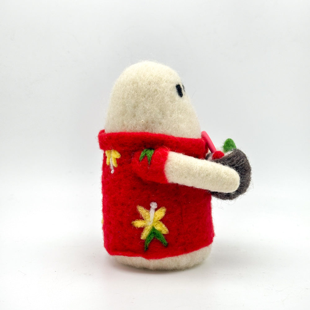 Image from the side of a small hand felted white ghost in a red Hawaiian style shirt holding a coconut cocktail